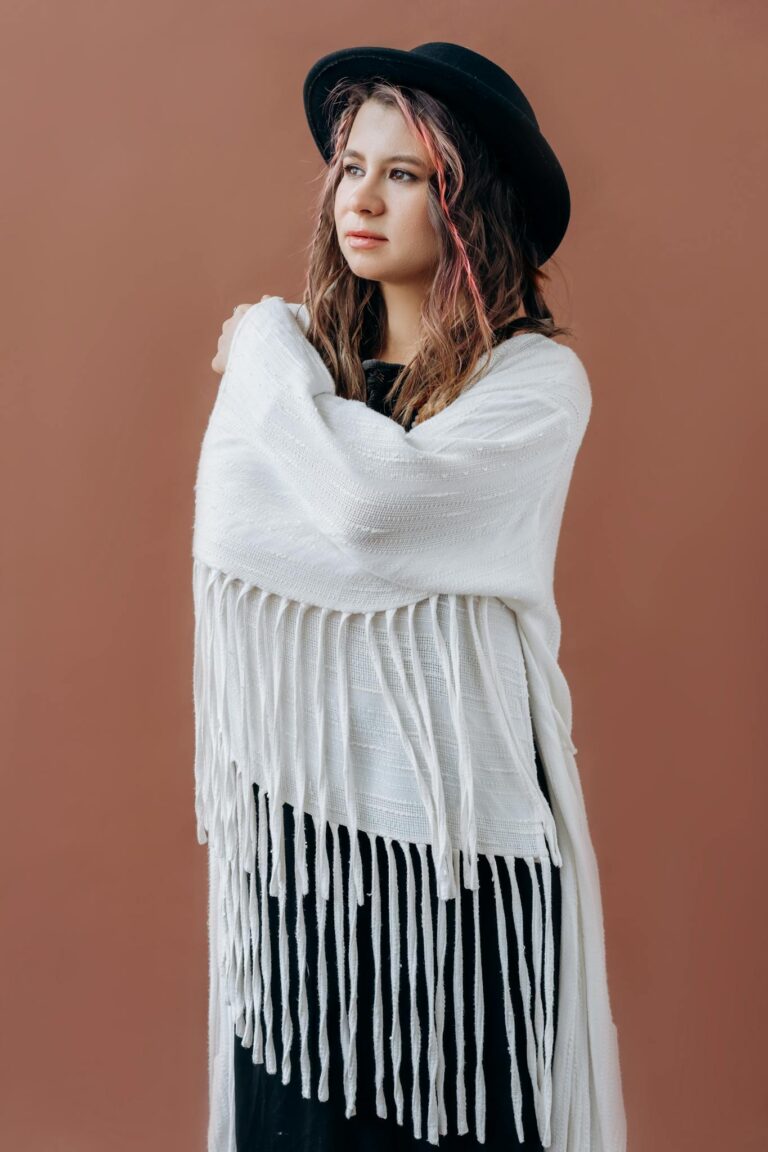 Stylish woman in a white shawl and black hat against a brown background.